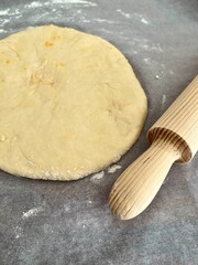 Dough with a wooden dough roller on a wooden board with baking parchment paper sprinkled with flour. Sieve flour, muffin, cake, roll out dough. Sift. Cooking process