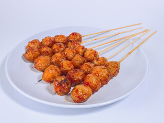 Grilled meatballs on skewers served on a white plate with spicy sauce, perfect for street food lovers and culinary presentations