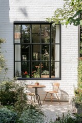 Charming garden area with a wooden table and chairs near a striking black-framed window surrounded by vibrant flowers during a sunny afternoon