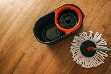 Plastic mop bucket and white spin mop on wooden floor, ready for house cleaning. Top view of cleaning equipment in natural light © shine.graphics