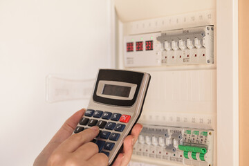 Calculating Home Electricity Bill. Woman calculating electricity usage with calculator near electric meter. Energy efficiency concept