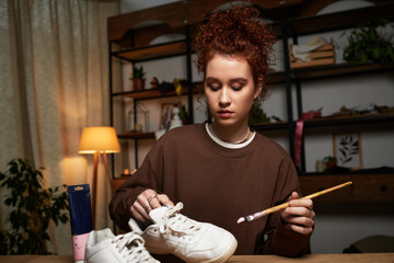 Creative young woman showcases DIY skills while customizing sneakers in modern craft space