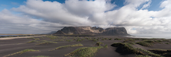 Wide-angle shot of Vestrahorn mountains emerging from mist with soft light illuminating black sand dunes and sparse vegetation on the Icelandic coast.