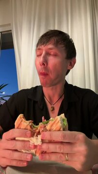 homem comendo hamburguer delicioso em casa 