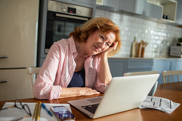Senior woman managing bills at home with laptop