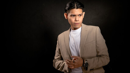 Asian man with glasses wearing beige blazer and white t-shirt standing confidently in studio with dark background, fingers forming a triangle, ideal for personal brand or leadership concept