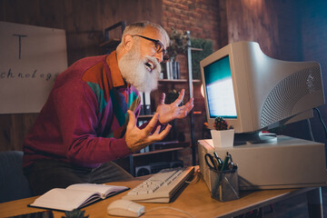 Senior man frustrated with outdated computer technology in office setting at night