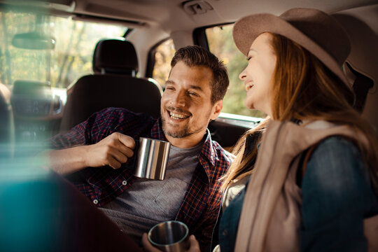 Happy couple drinking coffee and relaxing in the back of their car on a road trip