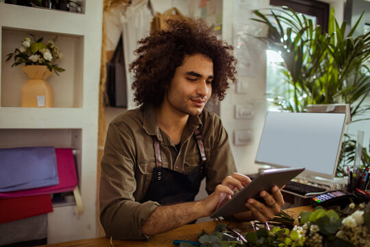 Young male florist using digital tablet at flower shop counter