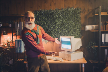 Elderly man showcasing vintage computer in warm office setting, embodying the nostalgia of early...