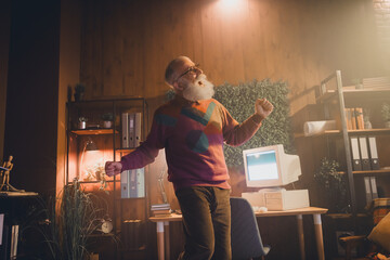 Elderly man enjoys music while working in a cozy home office featuring vintage computer setup and...
