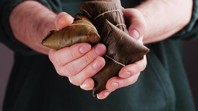 Hand holding zongzi (rice dumpling) with savoury fillings wrapped in bamboo or reed leaves.