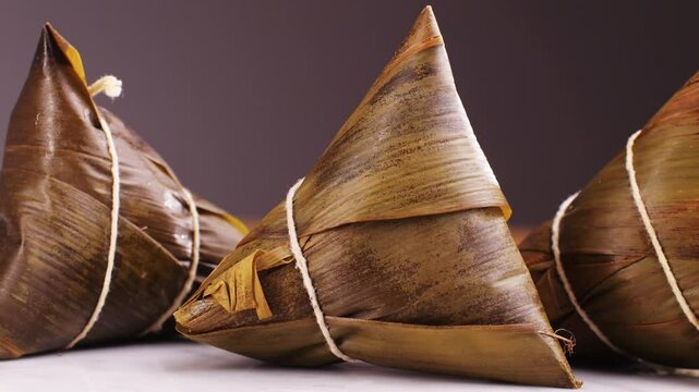 Hand holding zongzi (rice dumpling) with savoury fillings wrapped in bamboo or reed leaves.