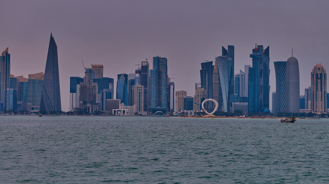 Doha Qatar skyline from corniche promenade sunset shot showing dhows in Arabic gulf with Qatar flag