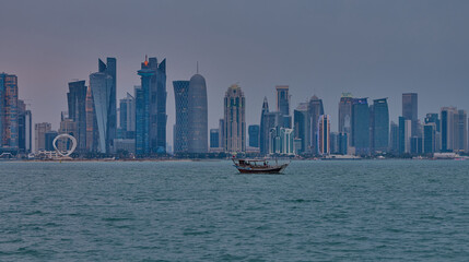 Fototapeta premium Doha Qatar skyline from corniche promenade sunset shot showing dhows in Arabic gulf with Qatar flag