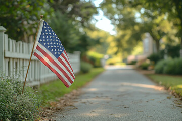 American flag waving near white picket fence along asphalt road, blurred background