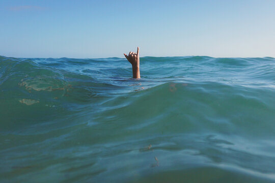 Teenage girl's hand reaching out of the ocean making a Hang Loose sign