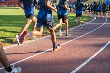 Group of athletes running on a track field in the morning, focus on legs and shoes, outdoor sports training, active and healthy lifestyle.