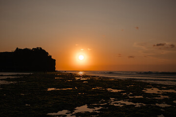 Bright orange sun at sunset against the background of the ocean. View from the beach to the evening sun and waves