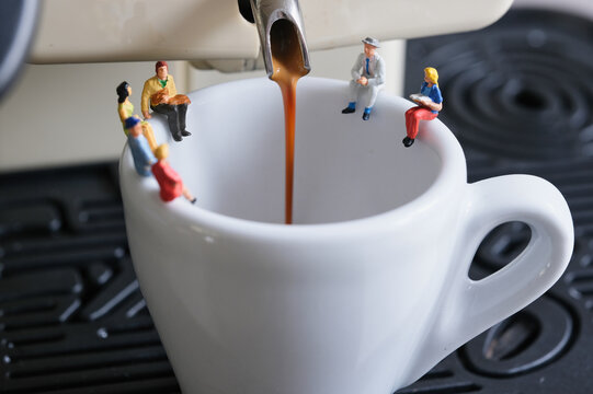 People sitting on a coffee cup while coffee is pouring, miniature figures scene