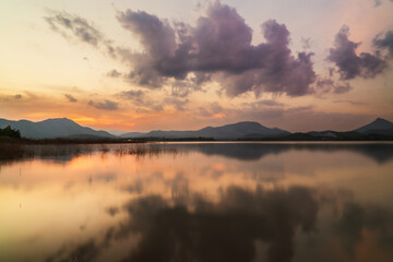 Sunset reflecting on calm lake with mountains and cloudy sky