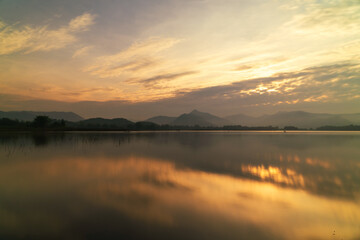 Sunset reflecting on calm lake with mountains and cloudy sky