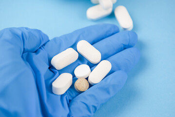 Close-up of hands of medical worker or pharmacist in blue latex protective gloves pouring white...