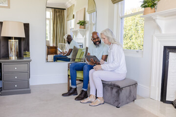 Interacting diverse senior couple using tablet in living room, with fireplace and wall mirror