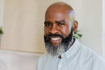 Smiling mature african american man wearing button-up shirt standing indoors with potted plant