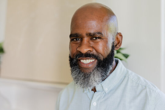 Smiling mature african american man wearing button-up shirt standing indoors with potted plant