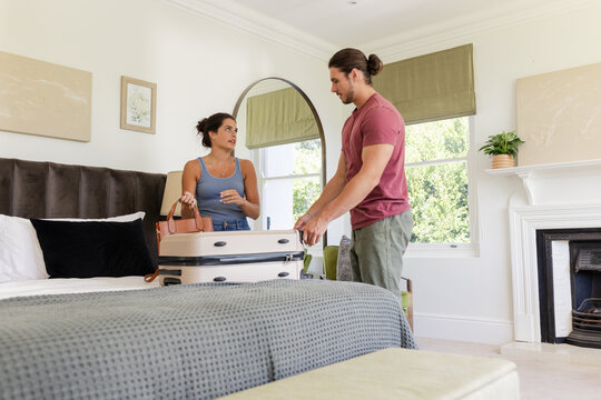 Unpacking couple organizing clothes on bed in bright furnished bedroom, with suitcase and handbag