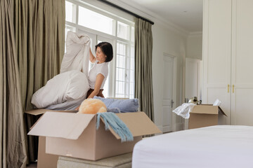 Moving in, asian korean woman arranging duvet cover and pillows in bedroom, with boxes, copy space