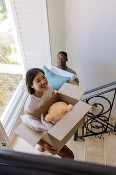 Moving in, diverse friends climbing staircase at home, with cardboard box