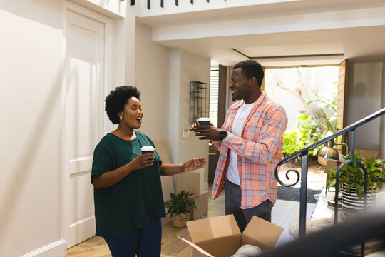 Sharing African American couple exchanging coffee cups in home entryway, with moving box and plants - Powered by Adobe