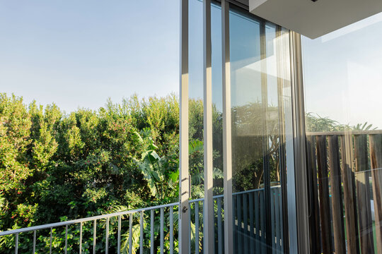 Sliding glass door is revealing balcony railing while sunlight is highlighting green hedge outside