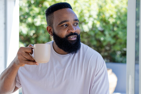 Mid-age African American man sitting near sunroom window, holding beige ceramic mug, copy space