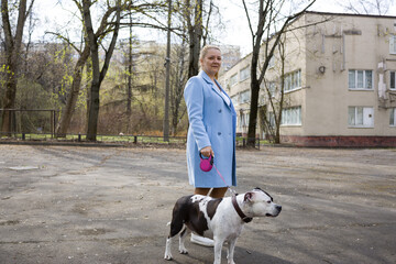 A woman in a blue coat walks a black and white dog on a leash