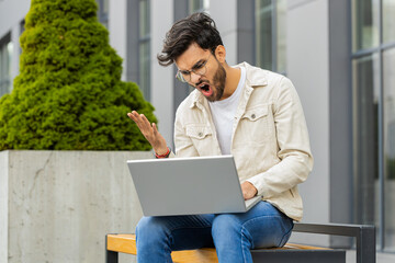 Displeased Indian man use laptop typing browsing working, loses becoming surprised sudden lottery...