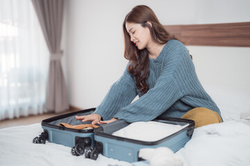 Young woman arranging clothes in a suitcase on the bed, preparing for a business trip or vacation while packing luggage in a cozy hotel room, embracing travel excitement