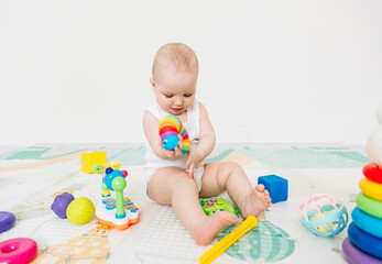 A 5-7 month old baby sits on the floor and plays with bright toys in his room.