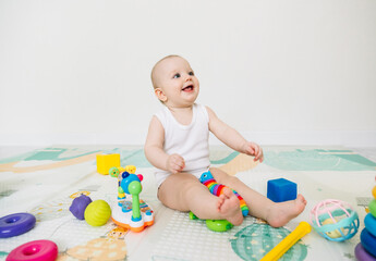 A 5-7 month old baby sits on the floor and plays with bright toys in his room.