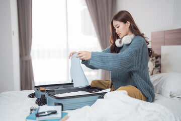 Young woman sitting on her bed, carefully organizing clothes and packing her suitcase, preparing for an exciting journey filled with adventure and new experiences