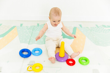 A 5-7 month old baby sits on the floor and plays with bright toys in his room.