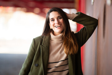 Smiling woman in green coat leaning against a wall