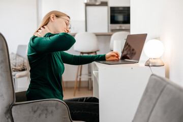 Young woman taking off glasses and suffering from neck pain at home office
