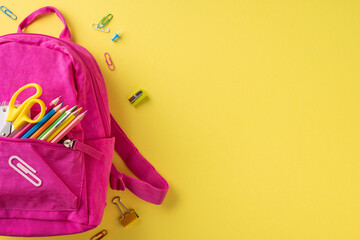 A vibrant pink backpack filled with colorful school supplies lying on a yellow backdrop