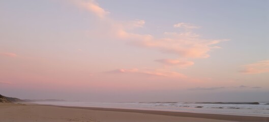 Serene beach at dusk with soft pastel clouds and gentle ocean waves.