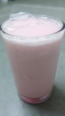 A chilled glass of smooth, creamy pink milkshake, topped with ice cubes. Its fruity color and frothy texture hint at a delicious strawberry or berry flavor, perfect for a summer refresh.