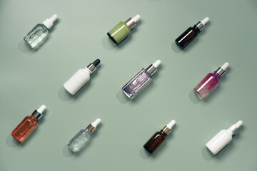 Naklejka premium Different glass bottles with serum or oil on green background. Trending shadow. Cosmetic mockup. Top view with copy space. Flat lay.