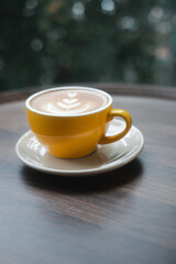 Close-up of hot cappuccino with beautiful latte art in yellow ceramic cup on wooden table.
